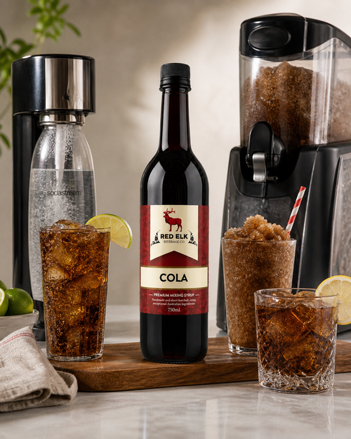 Red Elk Cola bottle with glasses of cola and a blender on a wooden board.